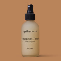 A frosted bottle of Gatherwise Hydration Toner with a black spray nozzle, centered against a solid warm tan background.