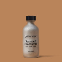 A bottle of Gatherwise Seaweed Face Scrub and Gentle Mask, featuring a frosted bottle and a black cap, set against a solid warm brown background.