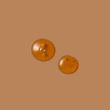 Two round amber-colored drops of Gatherwise Serious Eye Oil on a warm brown background.
